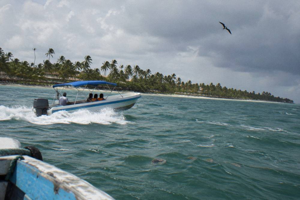 Speedboat crossing open water toward a green island coastline under scattered clouds